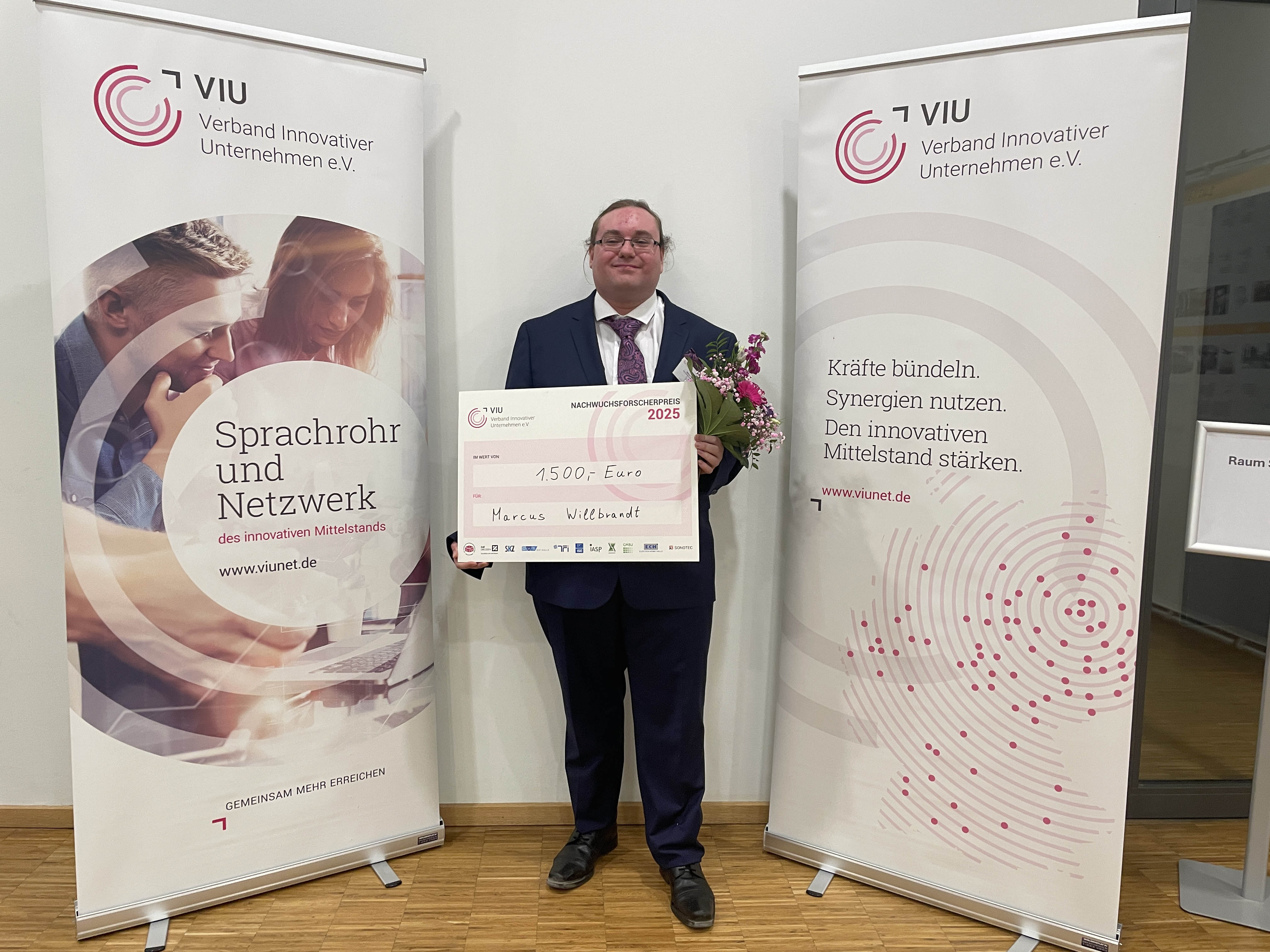 Marcus Willbrandt zwischen zwei Aufstellern in Berlin während der Preisverleihung