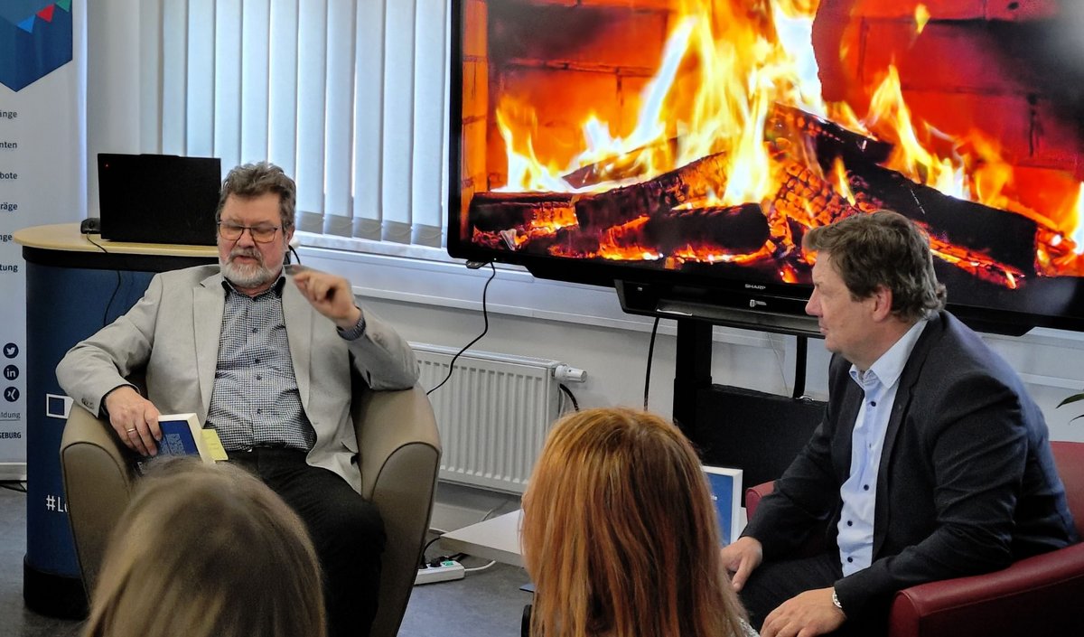 Prof. Kirbs links, Prof. Krabbes rechts sitzend vor dem digitalen Kaminfeuer im Gartenhaus
