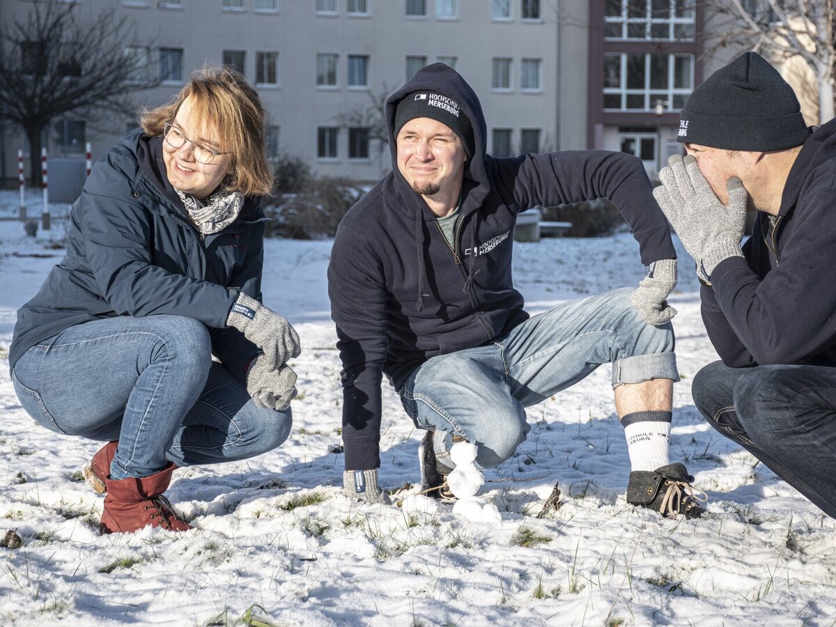 Drei Personen im Schnee hockend und präsentieren die Winterkollektion des Hochschulshops