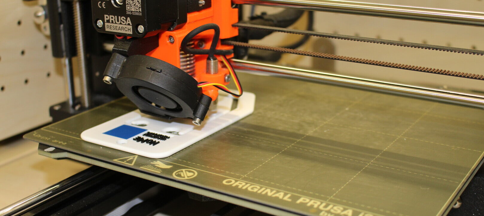 Zu sehen ist ein 3D-Drucker, welcher mit weißem Filament ein Produkt druckt. 