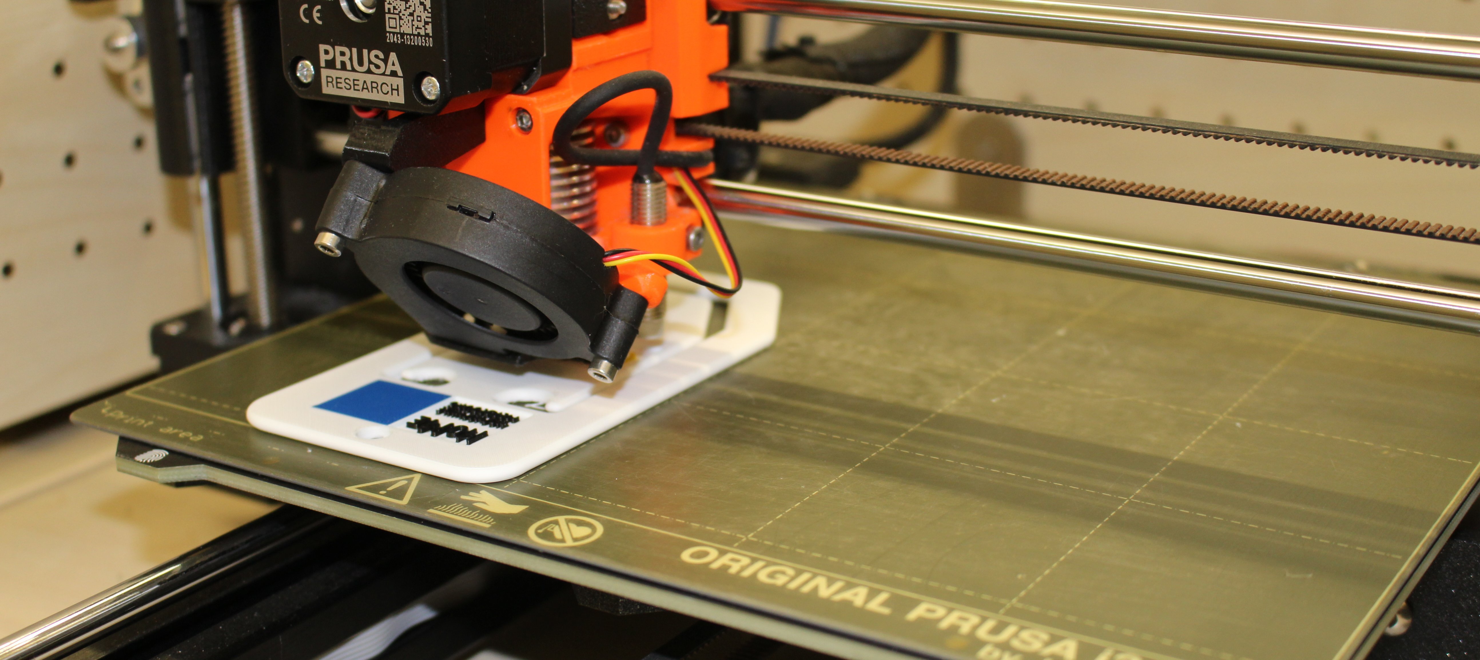 Zu sehen ist ein 3D-Drucker, welcher mit weißem Filament ein Produkt druckt.