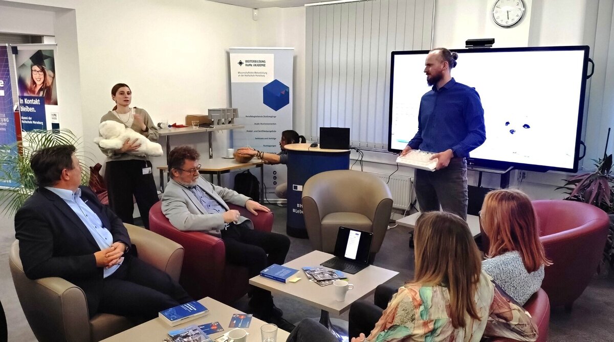 eine Miterabitende und ein Mitarbeiter vom Projekt stehend referieren vor sitzendem Publikum