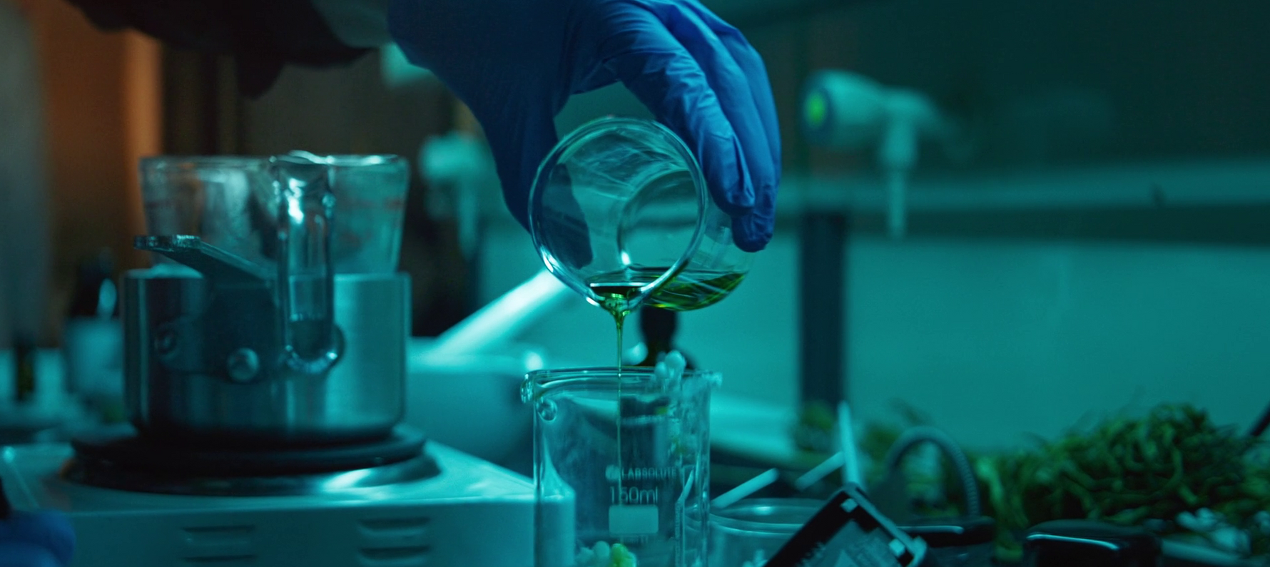 Hand mit Glas, dass eine gelbe Flüssigkeit in ein größeres Glas kippt