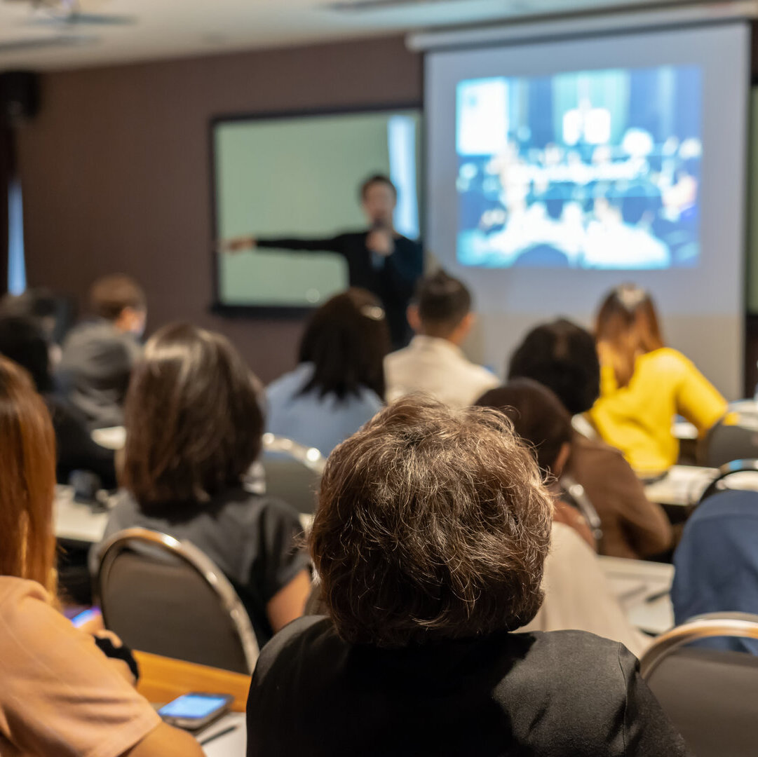 Person hält einen Vortrag vor einer Gruppe von Zuschauenden