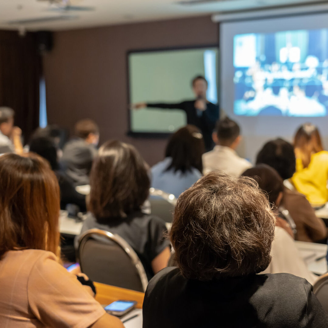 Person hält einen Vortrag vor einer Gruppe von Zuschauenden