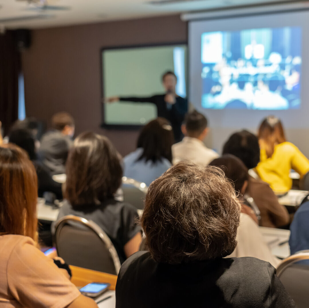 Person hält einen Vortrag vor einer Gruppe von Zuschauenden