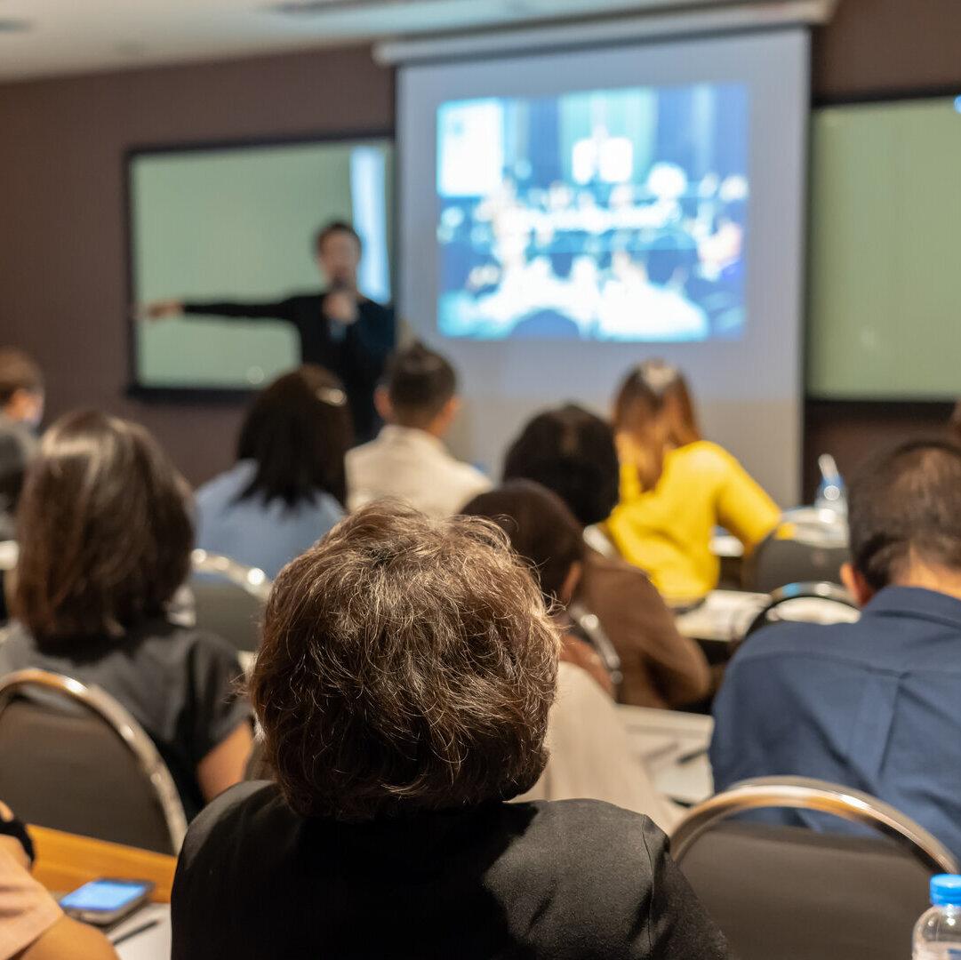 Person hält einen Vortrag vor einer Gruppe von Zuschauenden