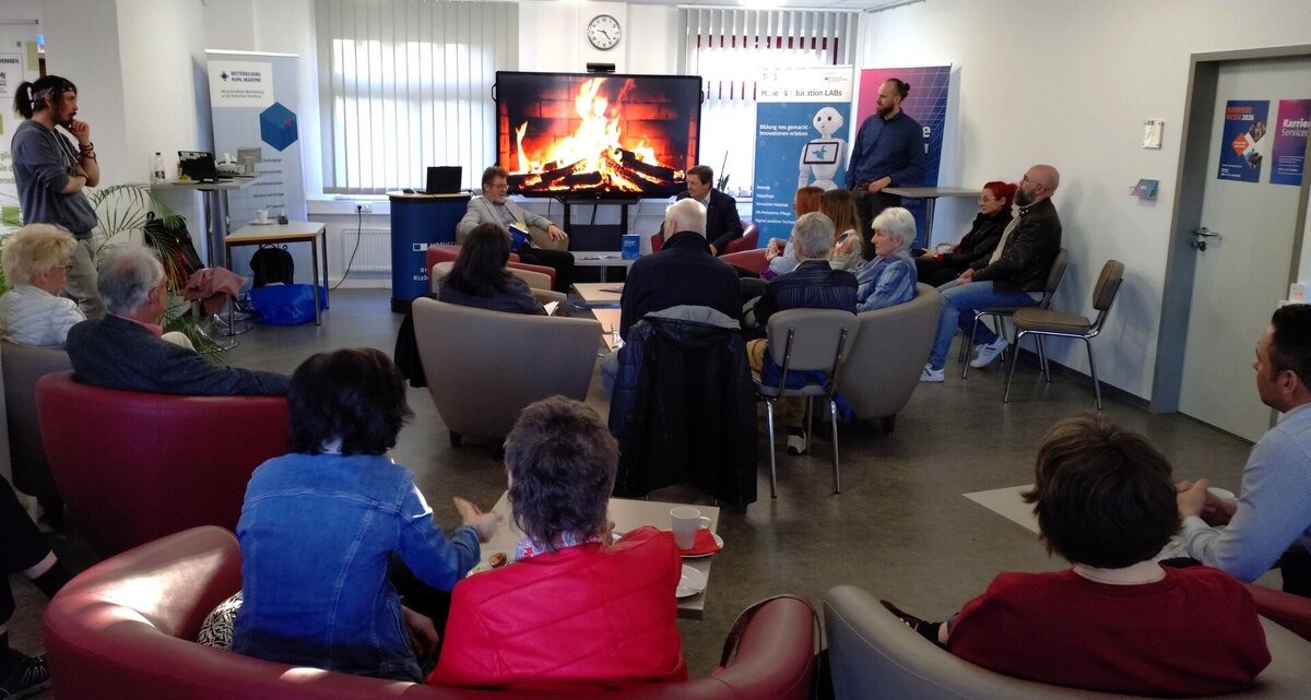 sitzende Teilnehmende in Sesseln hören aufmerksam dem Vortrag zu