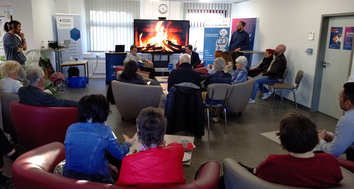 sitzende Teilnehmende in Sesseln hören aufmerksam dem Vortrag zu