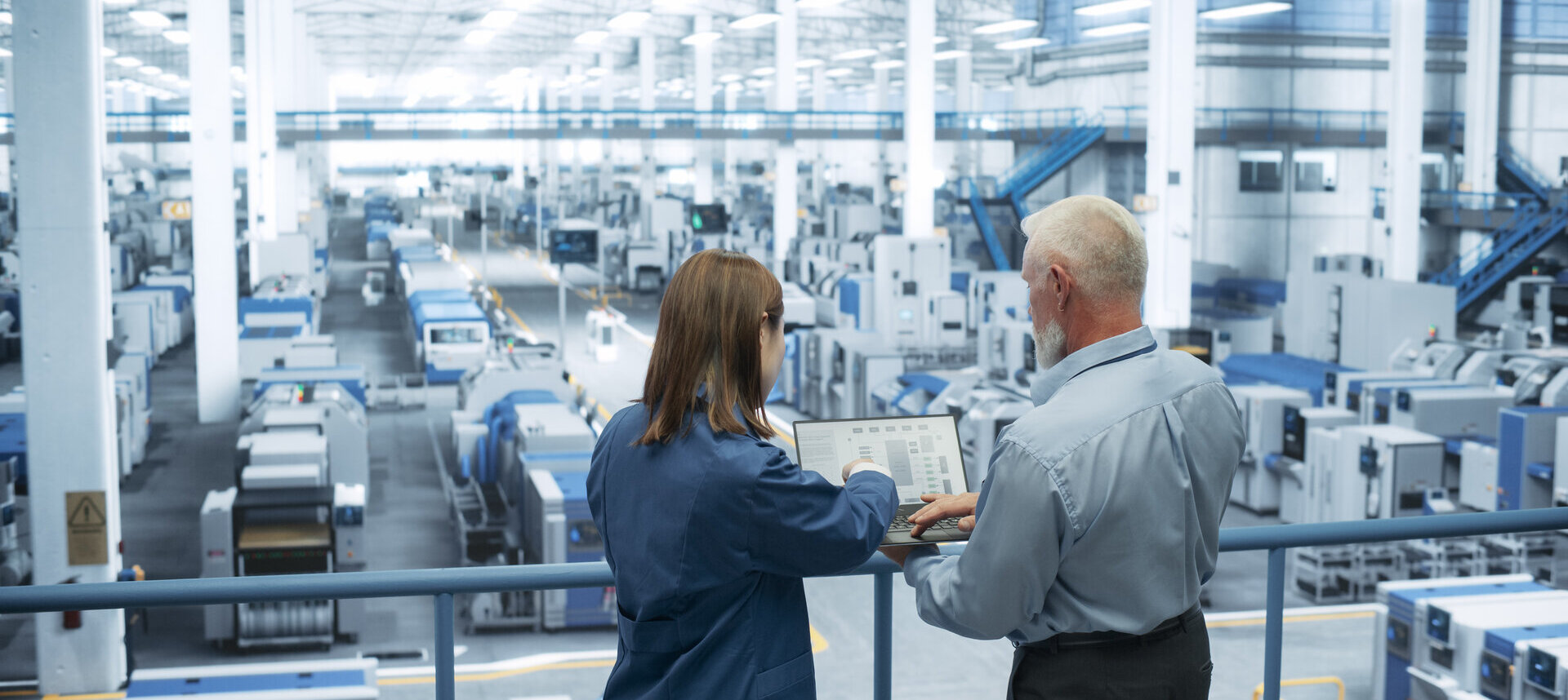 portrait-of-a-middle-aged-engineer-and-happy-asian-scientist-using-laptop-computer-and-talking-in-a-factory-facility-with-equipment-producing-modern-electronic-components-for-different-industries