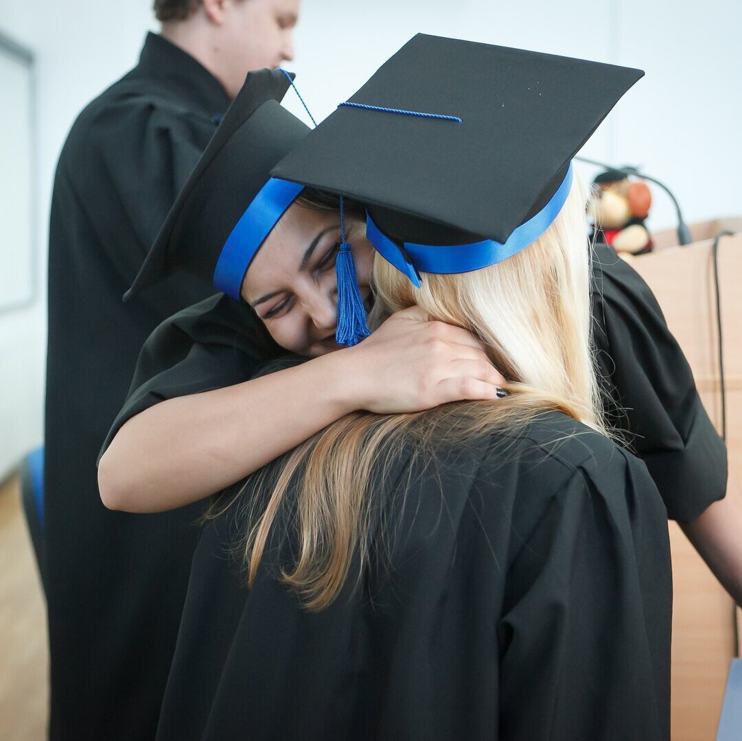 Zwei Personen umarmen sich freudig. Sie tragen Doktorhüte und Doktorroben