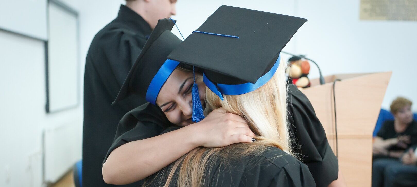 Zwei Personen umarmen sich freudig. Sie tragen Doktorhüte und Doktorroben