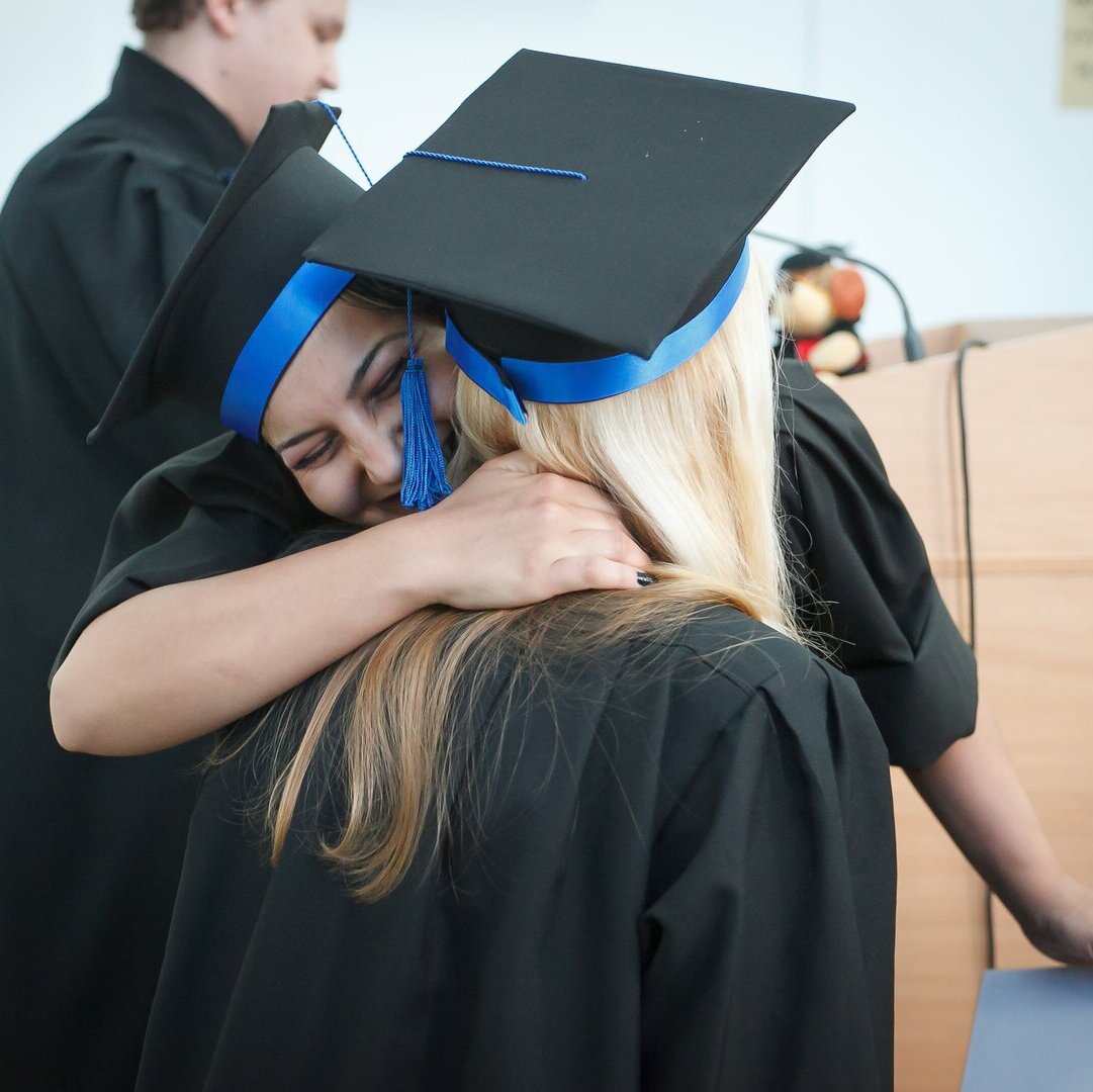 Zwei Personen umarmen sich freudig. Sie tragen Doktorhüte und Doktorroben