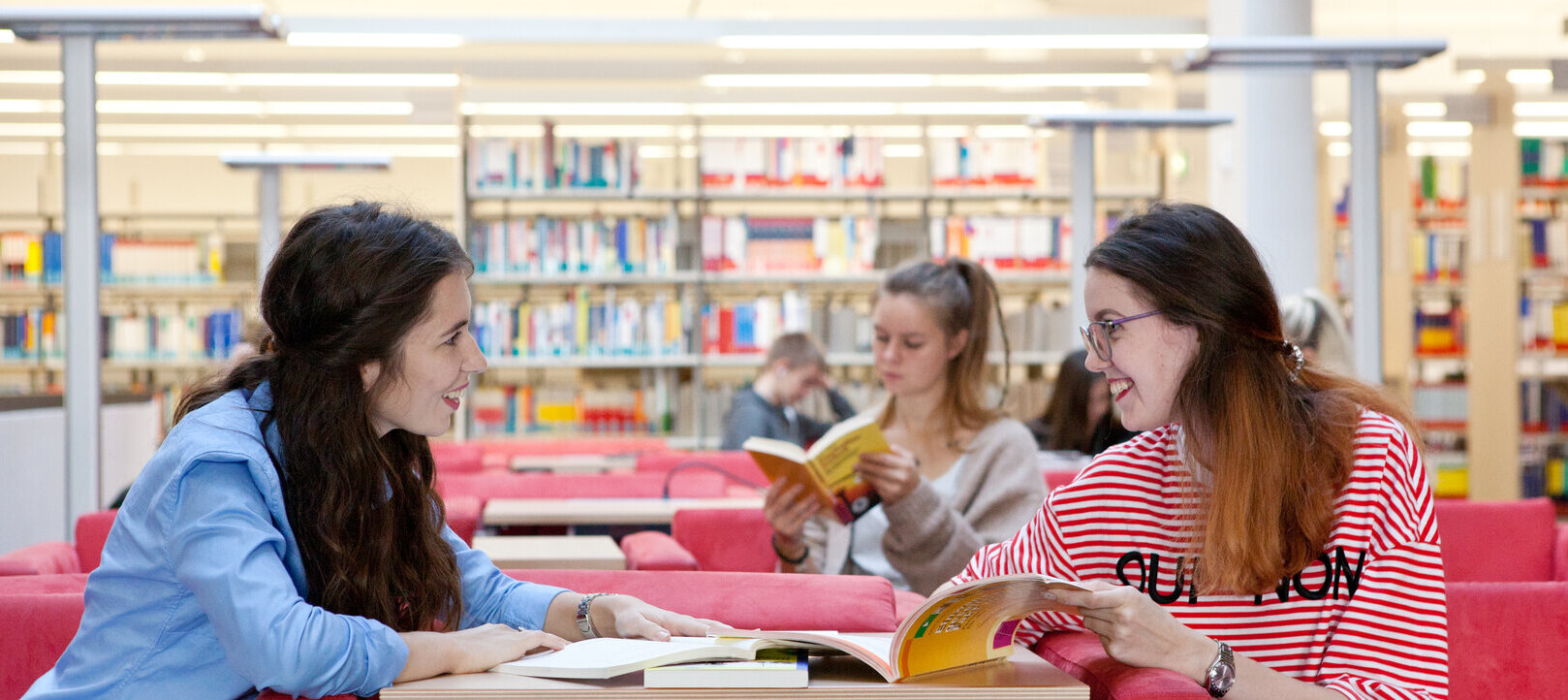 unterhaltende Studierende auf einer Couch der Hochschulbibliothek, dazwischen ein Tisch