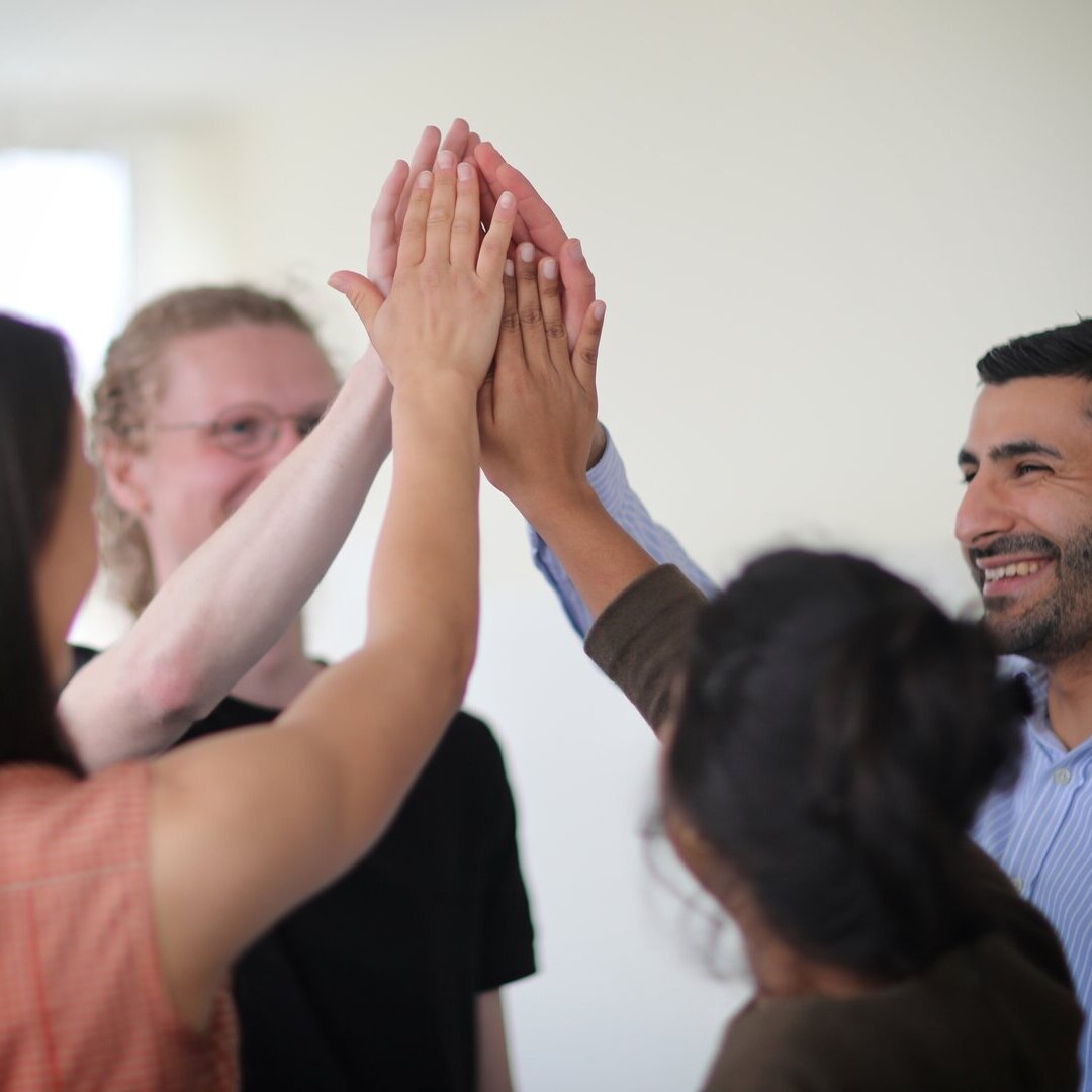 Vier Menschen halten ihre rechte Hand in der Luft zusammen
