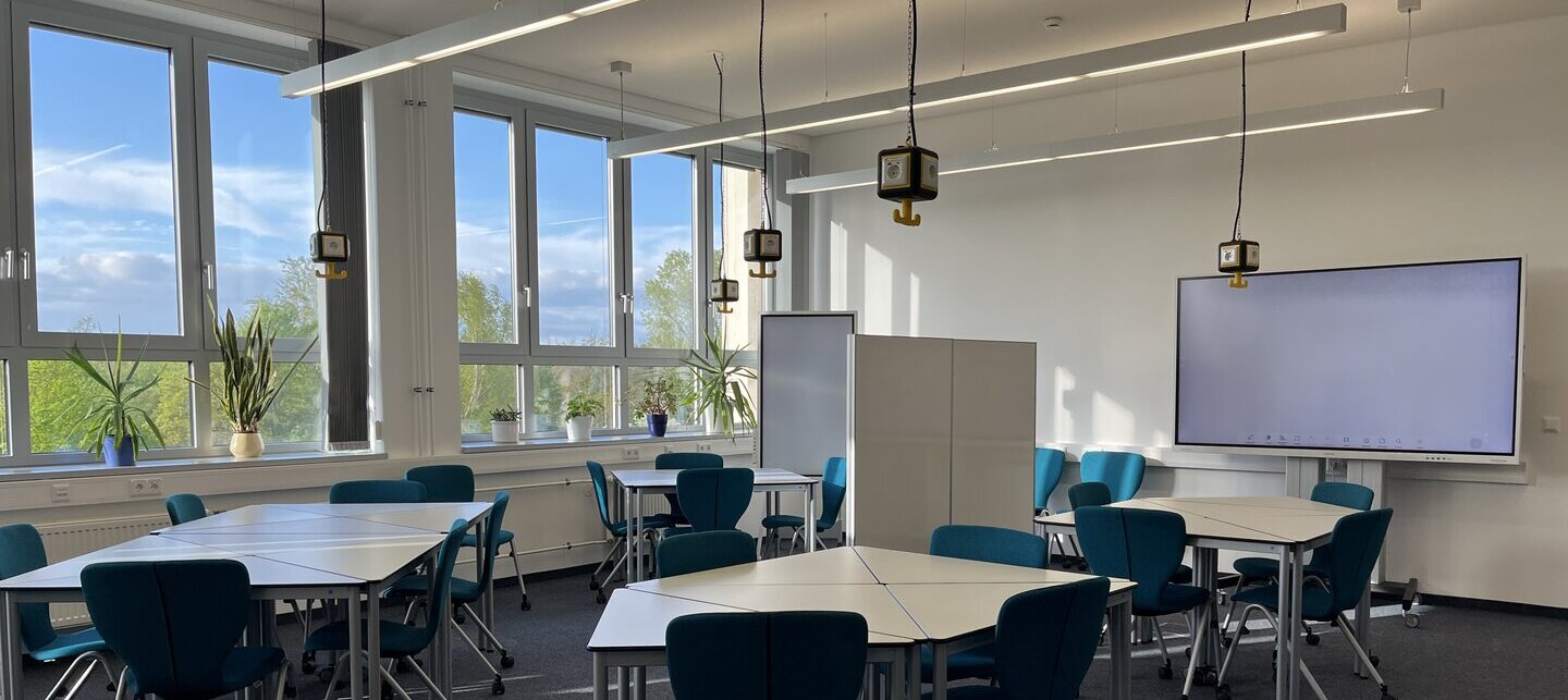 Foto des Active Laerning Room der Hochschulbibliothek mit Stühlen und Tischen und eines grßen Displays