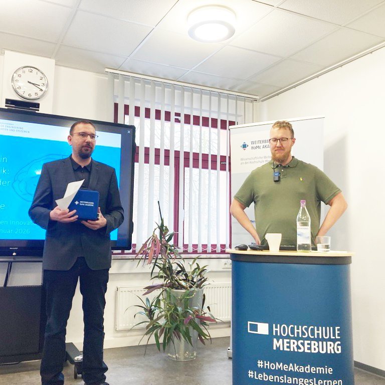 Zu sehen sind zwei Männer, einer von Ihnen spricht ein paar einleitende Wort und der Referent steht daneben.