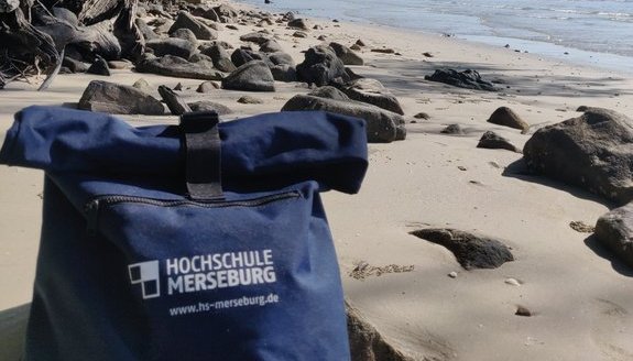 Rucksack der Hochschule Merseburg an einem Sandstrand.