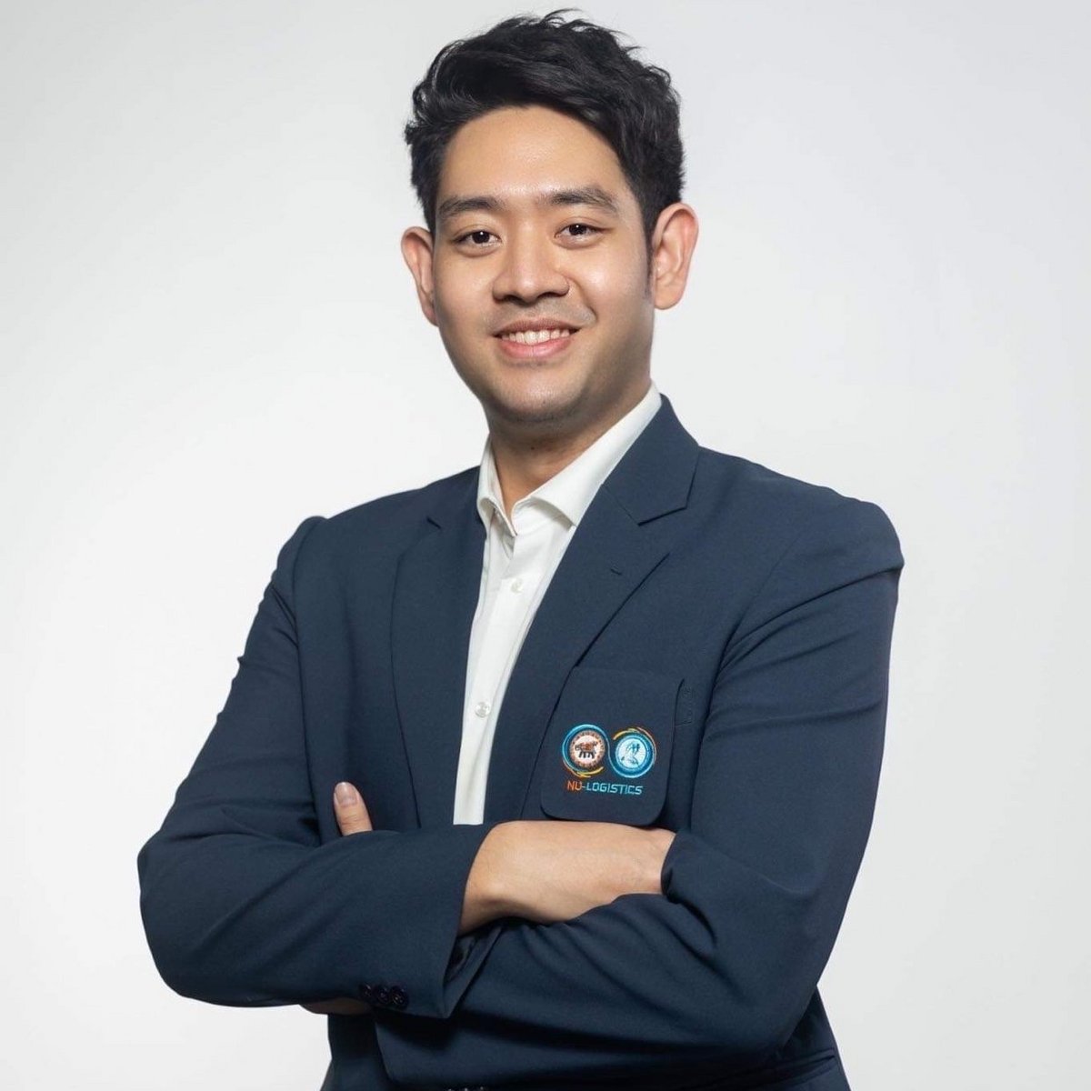 Ein Mann im Anzug schaut in die Kamera und lächelt. Seine Arme sind verschränkt.