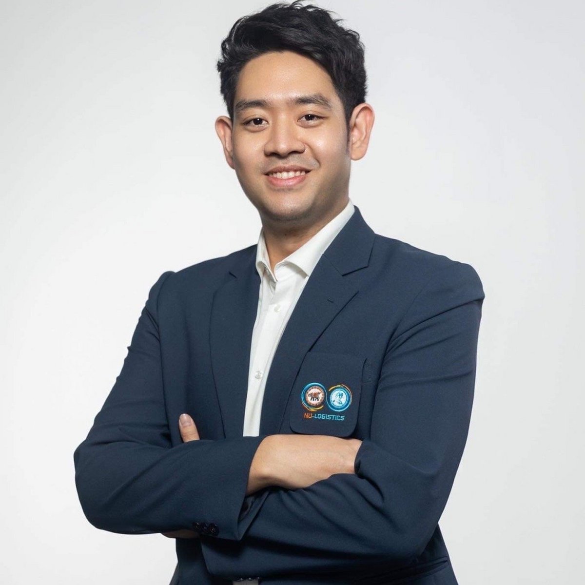 Ein Mann im Anzug schaut in die Kamera und lächelt. Seine Arme sind verschränkt.