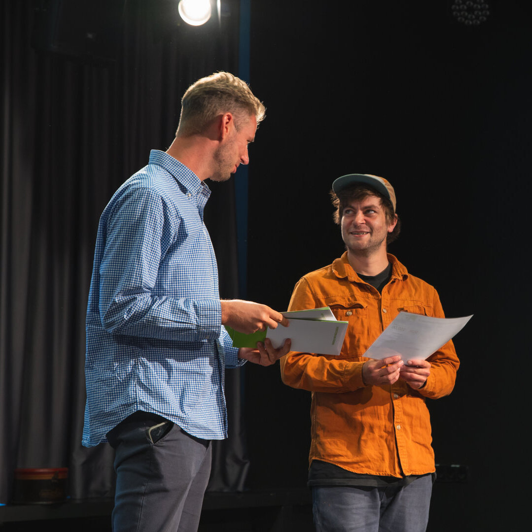 2 Personen in einem dunklem Raum mit Zeugnisübergabe