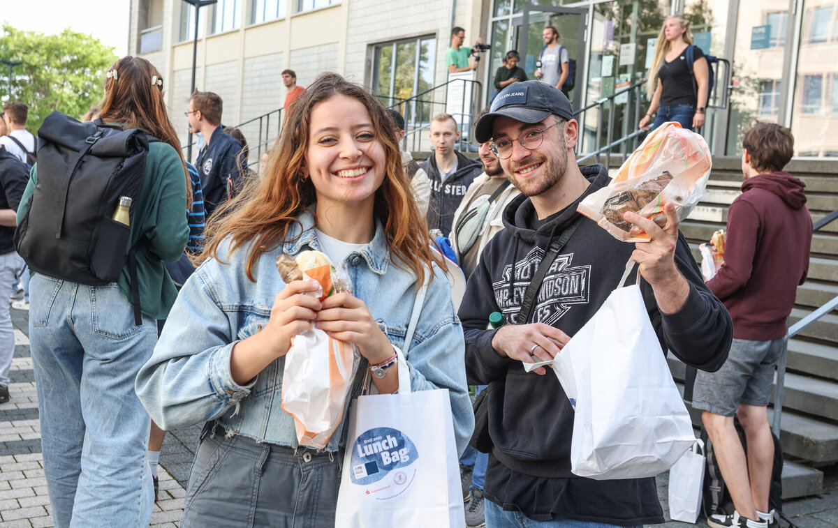 Zwei Studierende halten die Lunchbags für die Erstsemester und Brötchen in die Kamera.